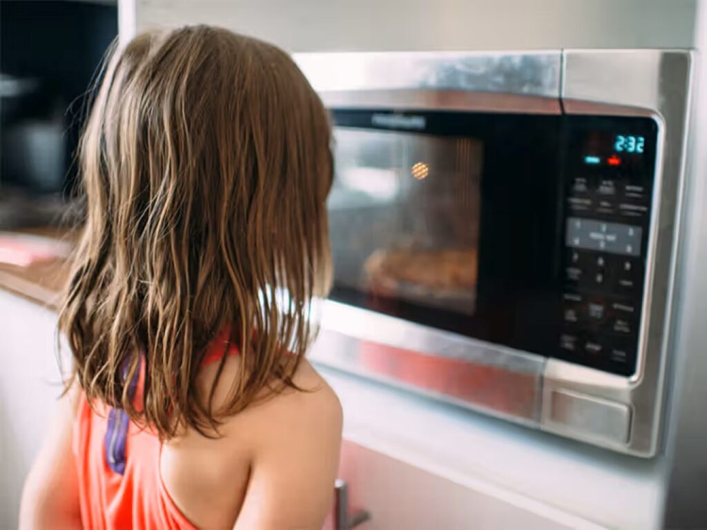 Youngster standing in front of a microwave oven window
