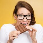 A woman in white taking a bite off a chocolate bar