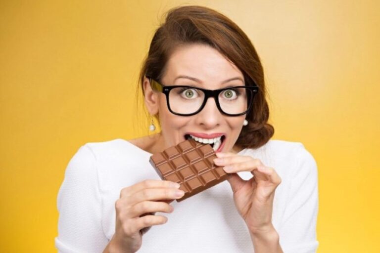 A woman in white taking a bite off a chocolate bar