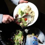 A kitchen staff member turning leftover food into a waste bin