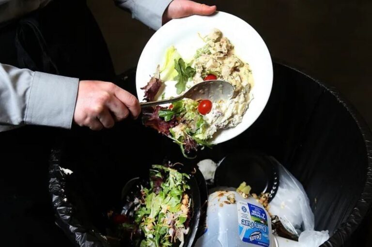 A kitchen staff member turning leftover food into a waste bin