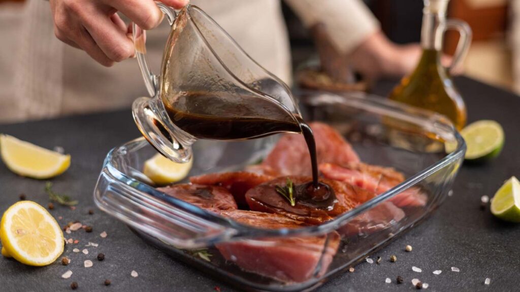 A woman pours soy sauce-based marinade into a glass cooking dish to marinate pieces of fresh tuna
