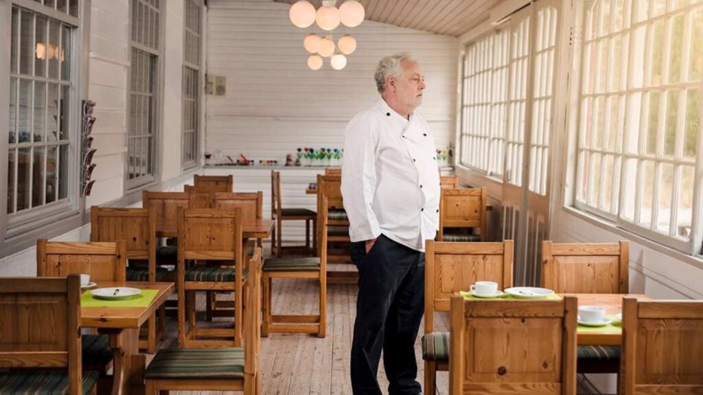 A chef standing in the empty dining area of a restaurant