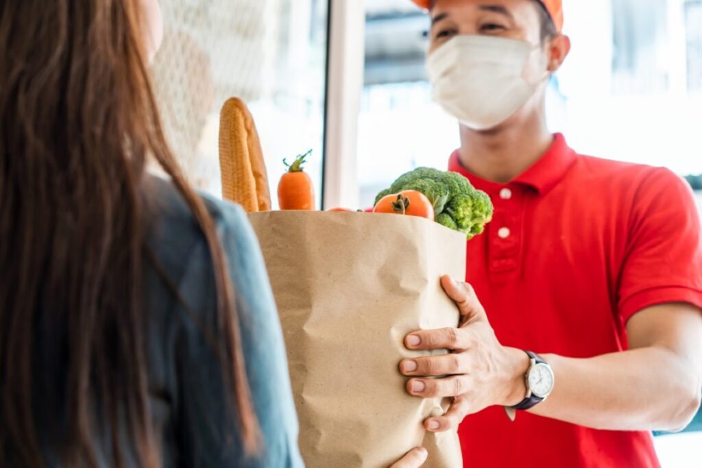 A food delivery agent handing a parcel of groceries to a customer
