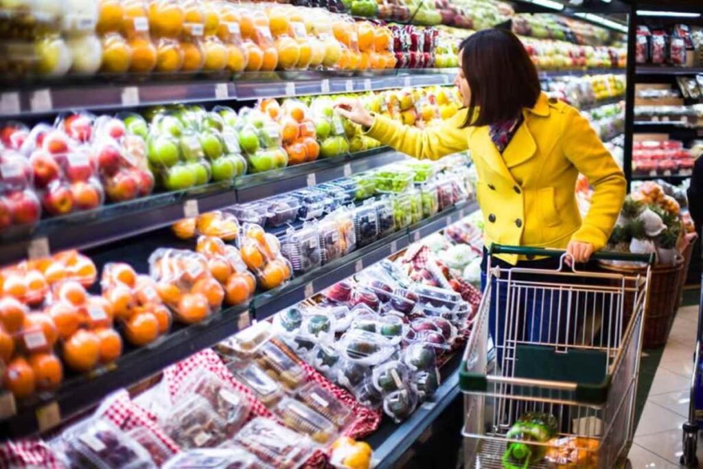 A woman inspecting a colorfully arranged supermarket shelf placement strategy of fruits