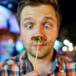 Caucasian young male eating a cricket at a night market in Thailand