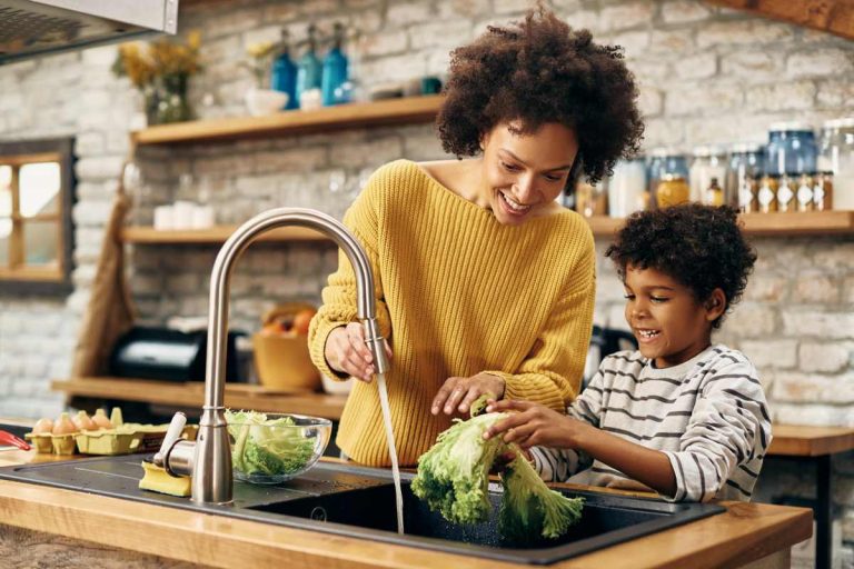 Happy black mother and son cleaning vegetables under the kitchen sink