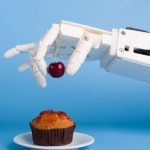 A robotic arm is placing a berry on a cupcake