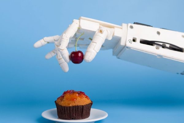 A robotic arm is placing a berry on a cupcake