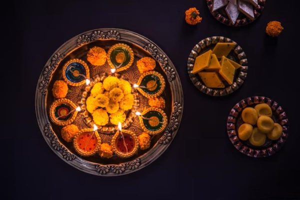 Happy Diwali - flower rangoli with sweets or mithai and diya in bowls for Diwali