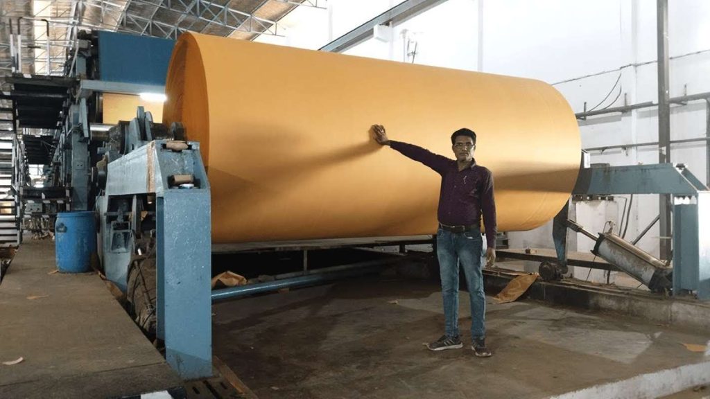 A man standing next to a giant roll of Kraft paper