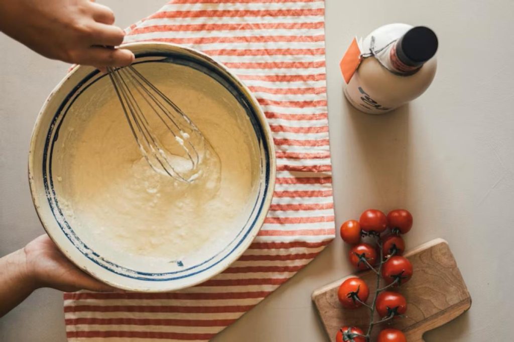 Hands whisking batter in a bowl with tomatoes nearby